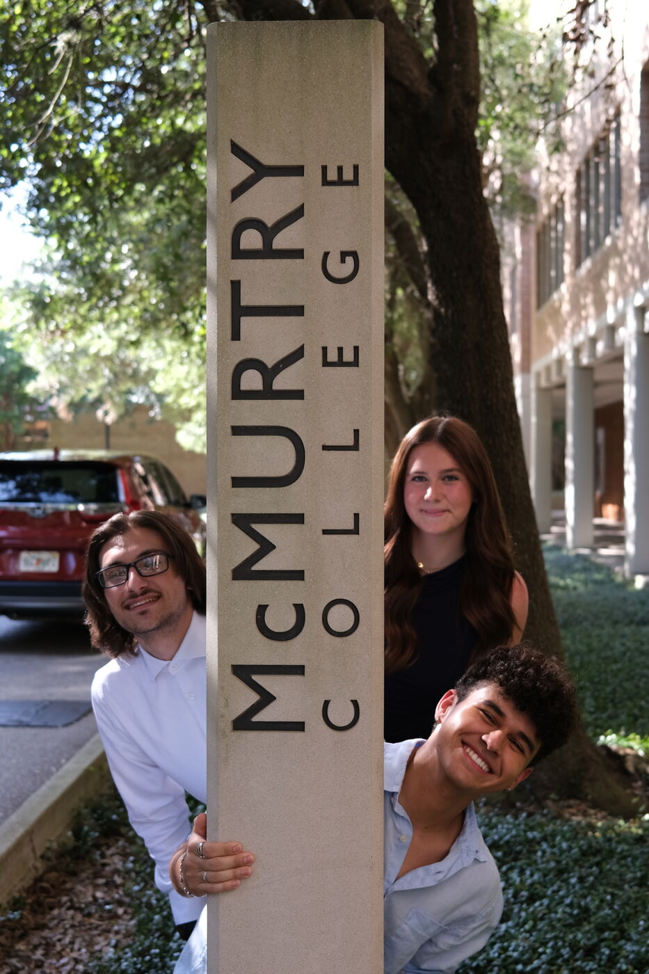 Ava, Chad, and Collin peeking out from behind the McMurtry College sign